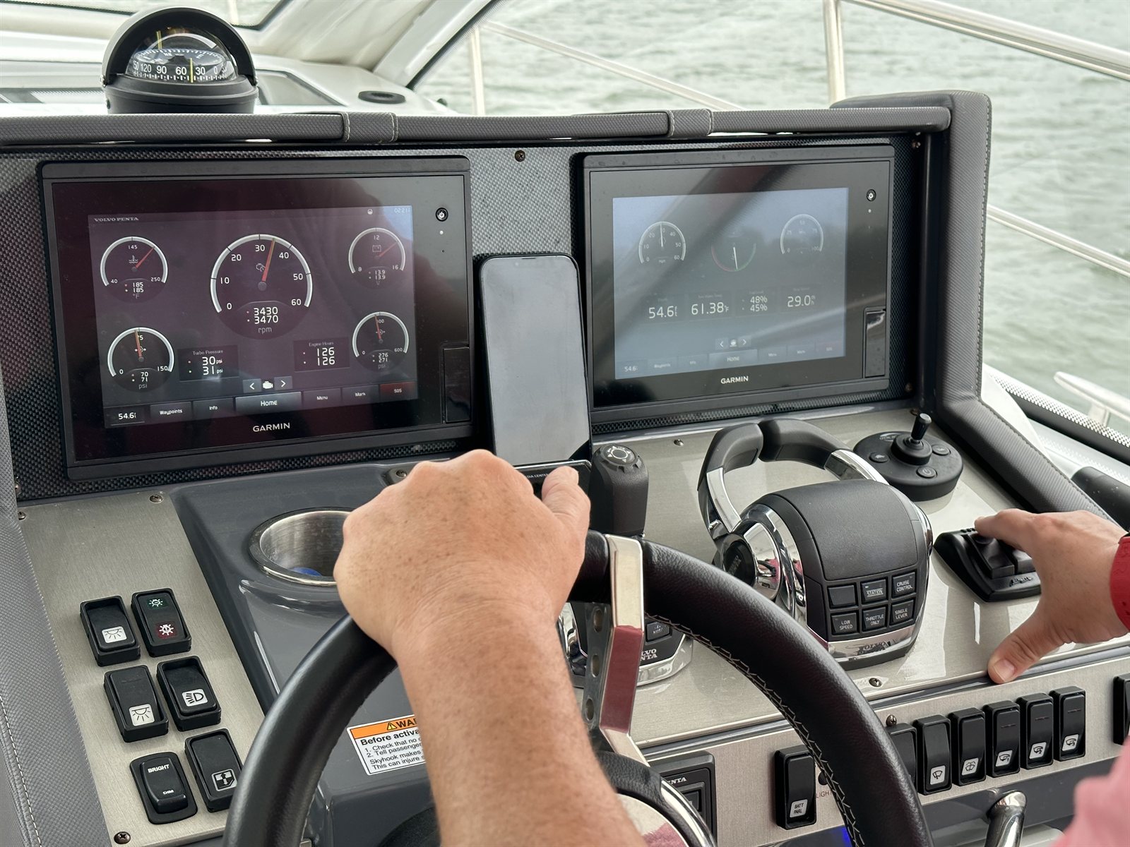 Hands on the wheel at a modern helm underway, with twin Garmin displays showing Volvo Penta engine data.
